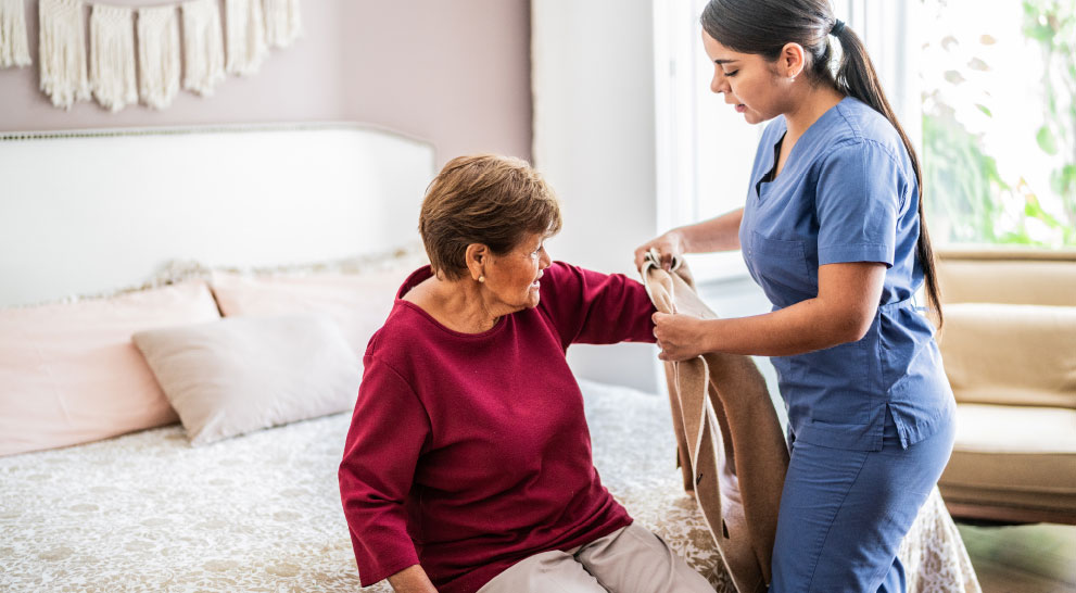 A nurse assists a senior woman put on a sweater.