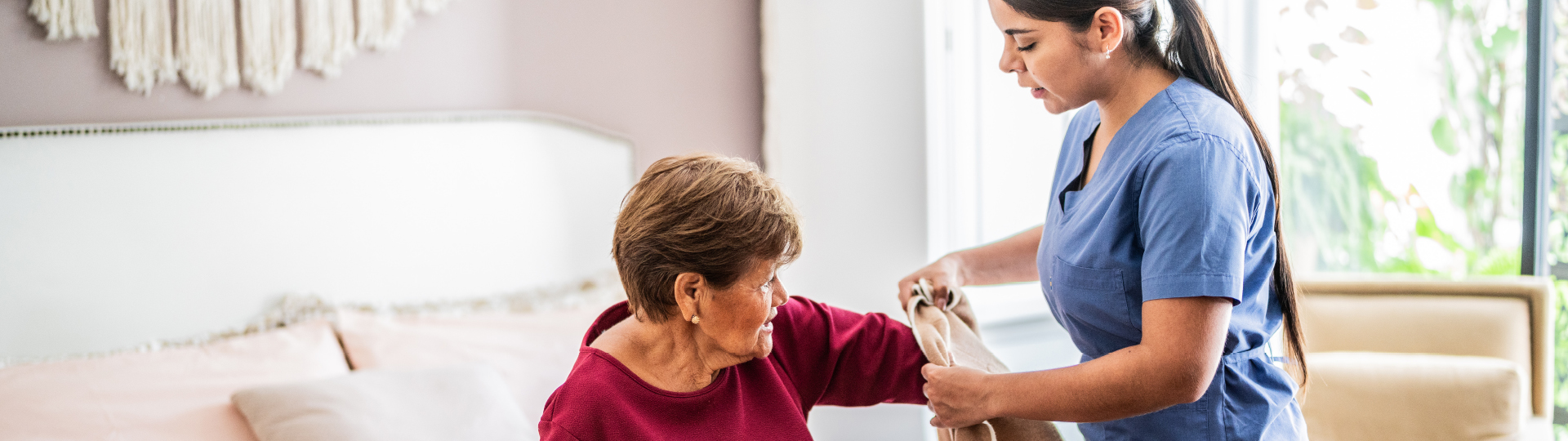 A nurse assists a senior woman with putting on a sweater.