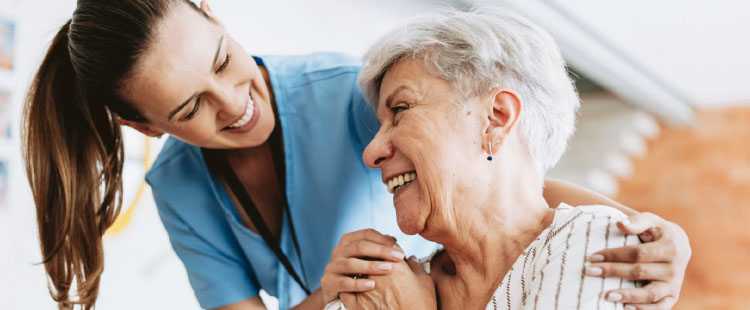 A nurse smiles at a senior woman as they stand next to one another.