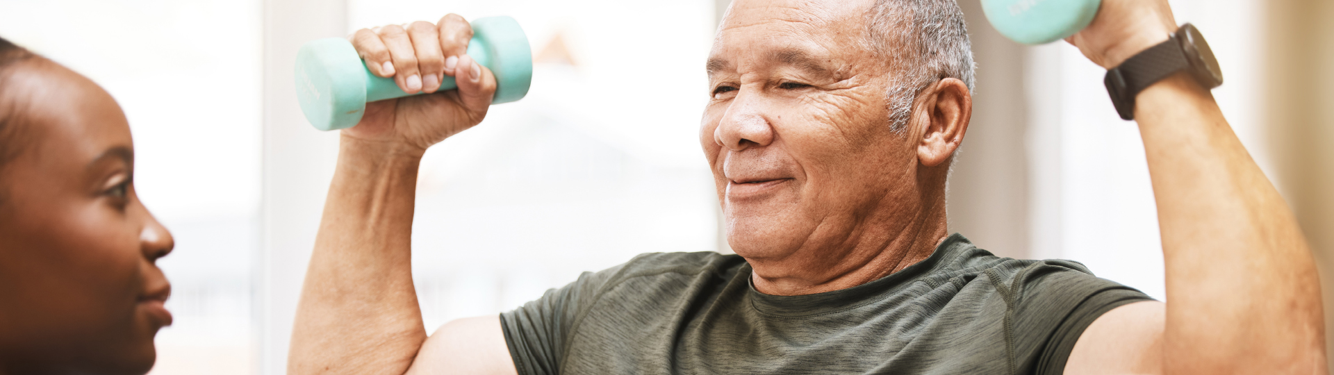 A senior man holds a weight over his head during a short-term rehab session.