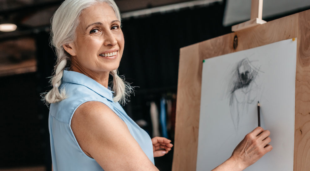 A senior woman paints and smiles to one side.