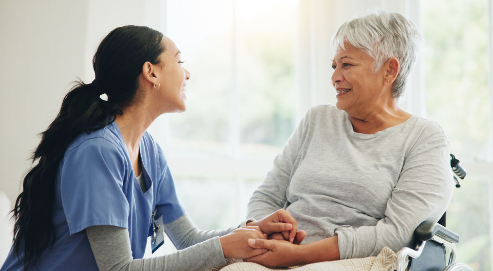 A nurse sits with a senior woman and smiles.