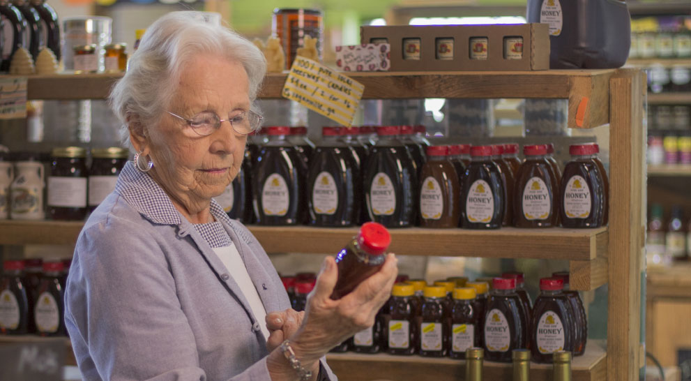 Older woman shopping in a store, looking at honey | Presbyterian Village Athens