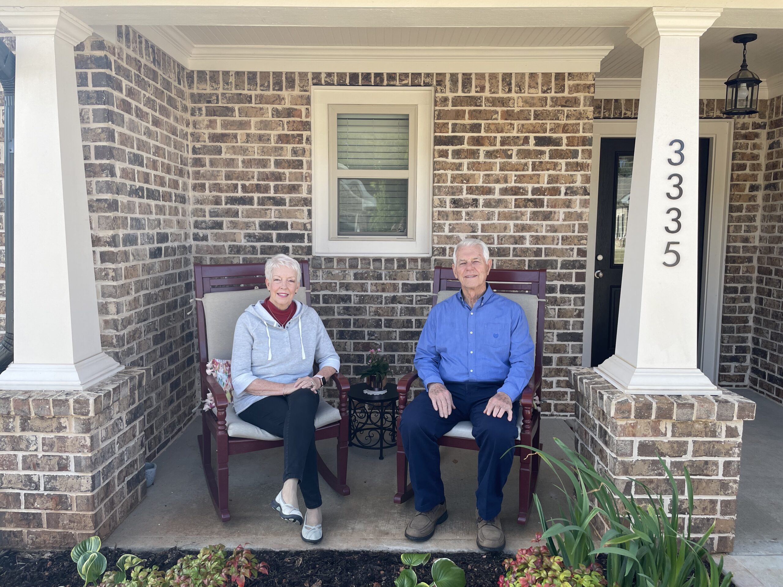 A senior man and woman sit on their front porch at a senior living community.